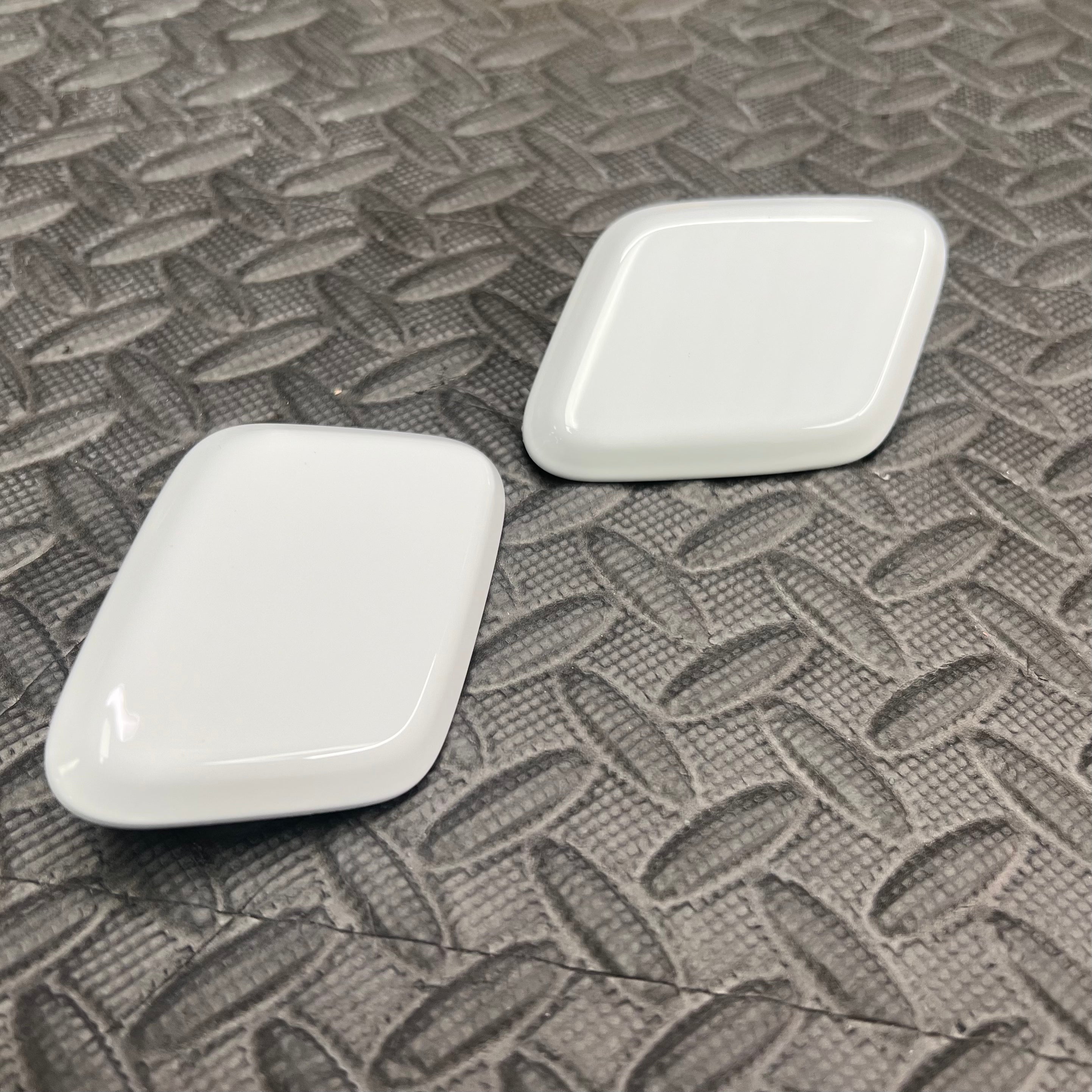 A pair of white Ford headlight washer covers placed on a textured surface.
